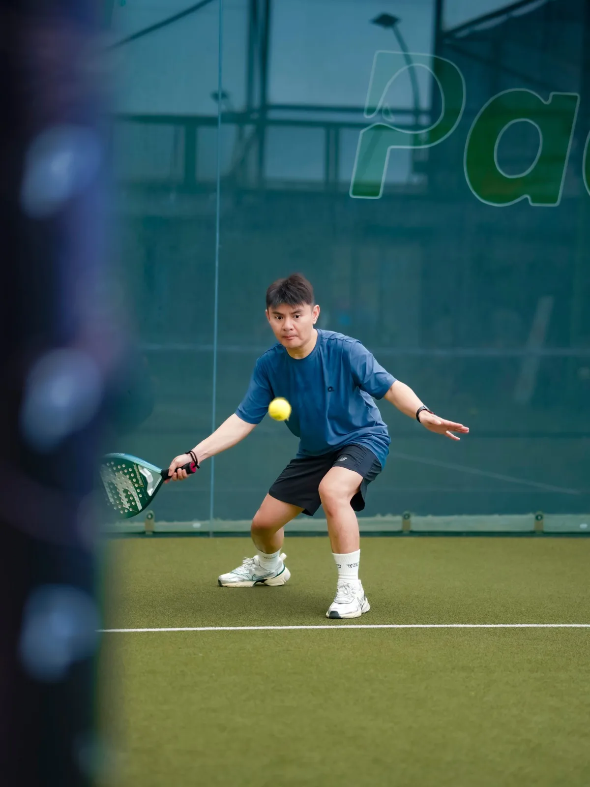 A padel player preparing to strike an overhead on an indoor court
