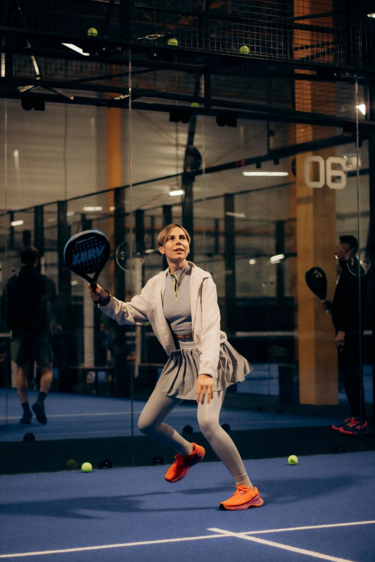 A woman preparing to play a padel ball beside the glass wall