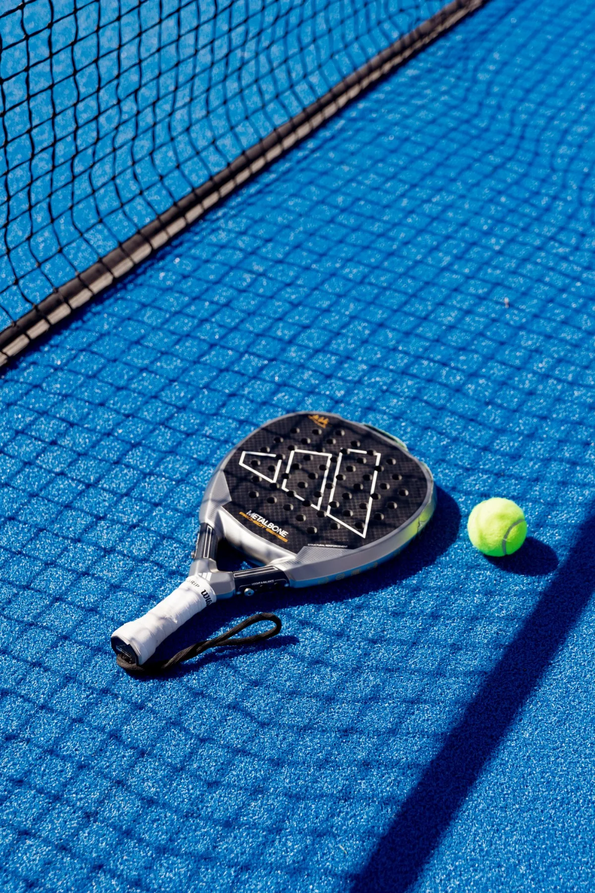 A padel racket and ball resting on a blue court